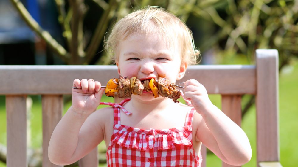 Young child eating a BBQ meat skewer.